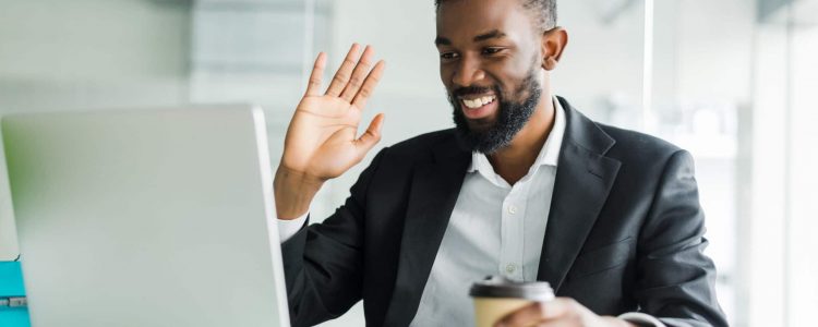 Young African manager with stubble sitting in front of open laptop wearing earphones while having video conference call with business partners