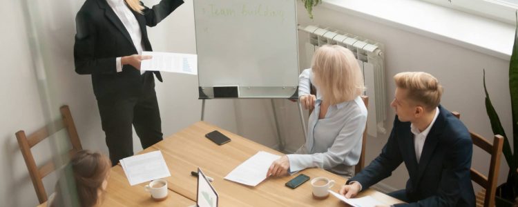 Businesswoman ceo boss in suit presenting corporate strategy pointing on flip chart at group meeting, business coach leader giving presentation explaining team goals in conference room at training