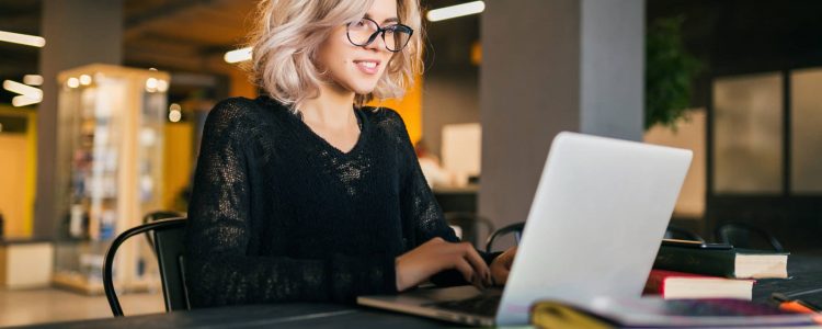 portrait of young pretty smiling woman sitting at table in black shirt working on laptop in co-working office, wearing glasses